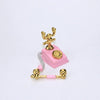A miniature vintage rotary desk phone decor featuring gold-colored components and pink plastic.