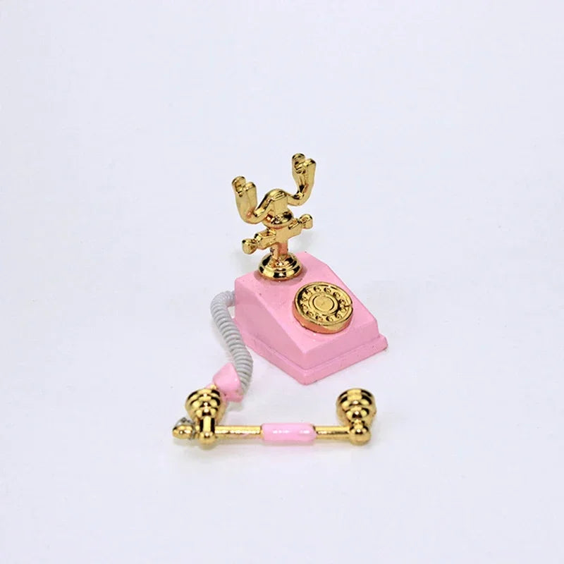 A miniature vintage rotary desk phone decor featuring gold-colored components and pink plastic.