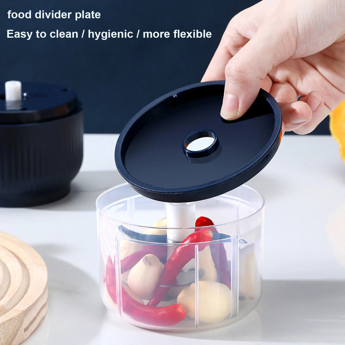 A hand is using a black food divider plate with a white blade to mince vegetables in a clear plastic container.
