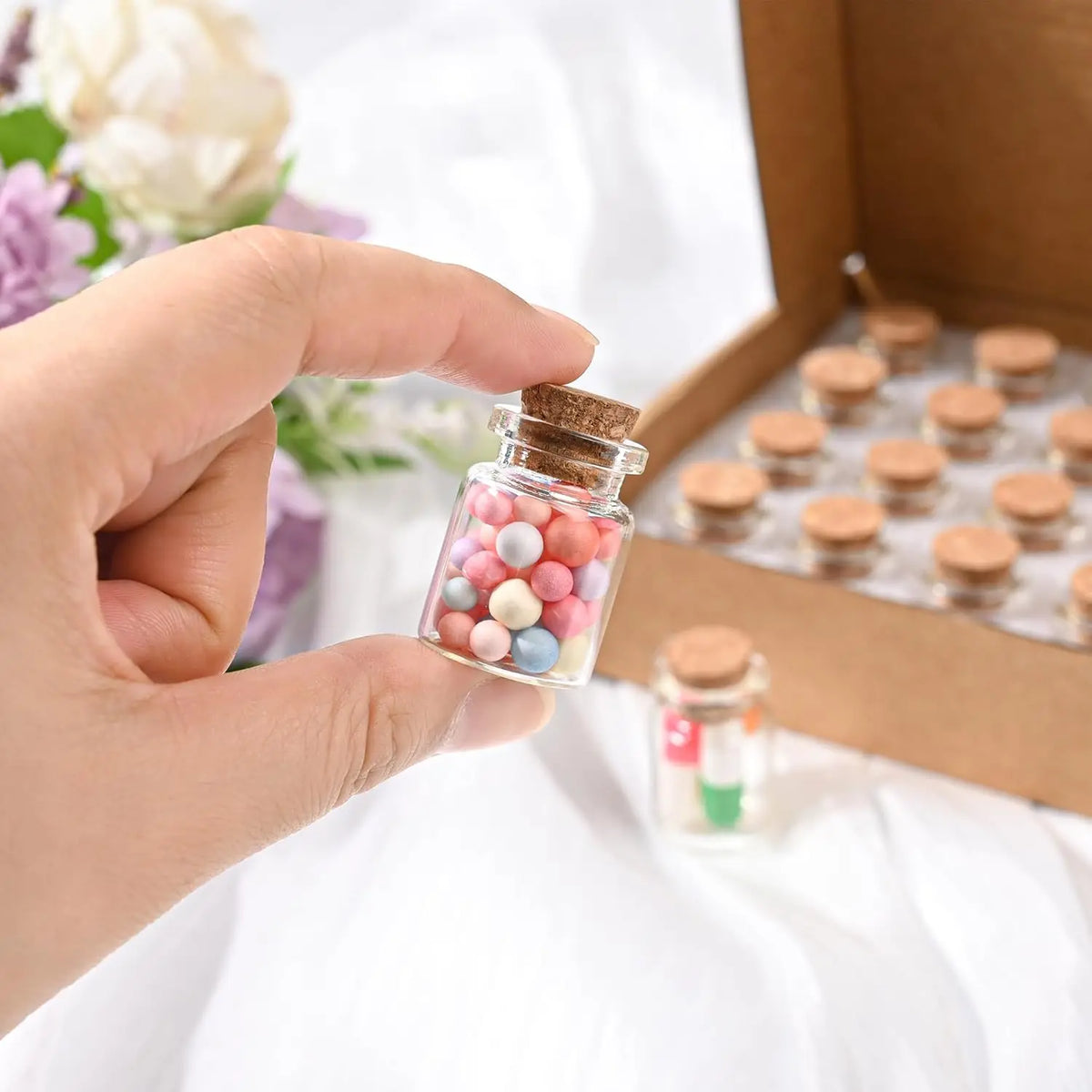 A hand holds a small glass jar filled with colorful cork stoppers for DIY decor inside a cardboard box.