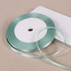 A spool of light mint green satin ribbon is shown on a white box, ready for gift wrapping or crafts.