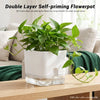 A white self-priming flowerpot filled with green plants sits in a clear glass base on a wooden table.