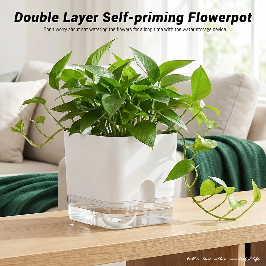A white self-priming flowerpot filled with green plants sits in a clear glass base on a wooden table.