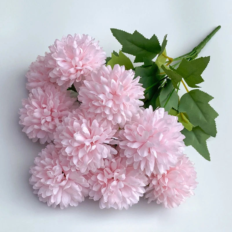 A bouquet of pink artificial hydrangea and camellia flowers with green leaves.