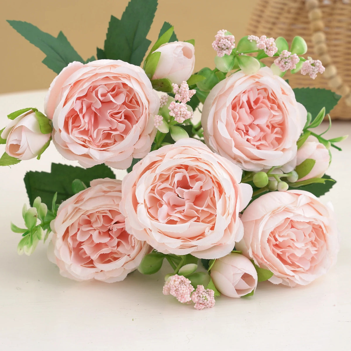 A bouquet of pink silk peony roses with green leaves and small pink filler flowers.