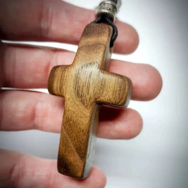 A handcrafted walnut cross keychain held between fingers.