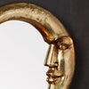 A close-up of a golden crescent decorative wall mirror with a stylized face design.