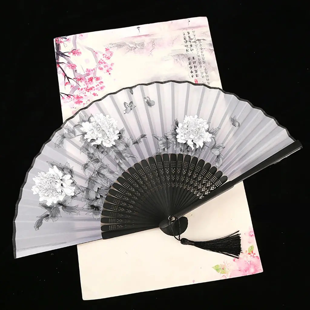 A vintage silk folding fan with delicate pink and white floral patterns is displayed against a light background.