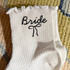 White knit socks with the word Bride embroidered on the foot section.