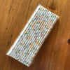 A pack of 100 colorful striped and polka dot paper drinking straws lying on a wooden surface.