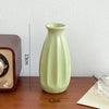 A light green ceramic bud vase with vertical ridges sits on a wooden surface.
