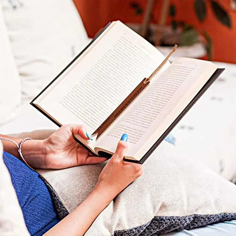 A person's hands are holding an open leather Bible with a bookmark inside, resting on a white pillow.