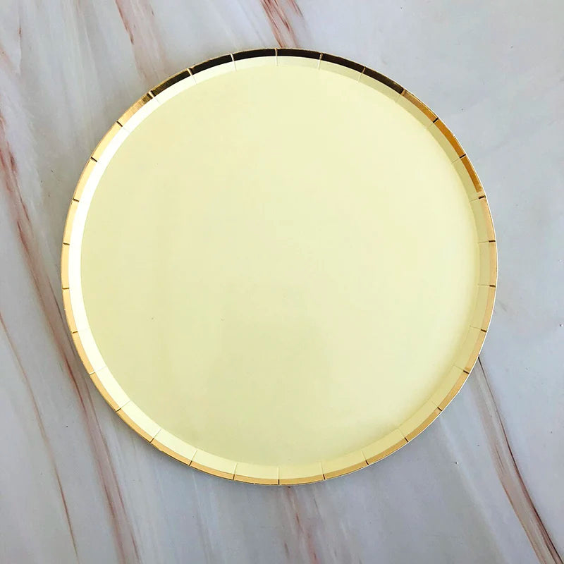 A round gold disposable party tableware set with plates resting on a marble surface.