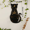 A black silhouette of a cat with a crescent moon and crystals on its body, displayed against a white wall.