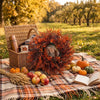 A large, textured wreath made of reddish-brown foliage rests on a plaid blanket outdoors.