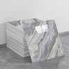 A stack of self-adhesive marble tile stickers featuring gray marble with yellow veining on a gray floor.