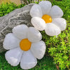 A cluster of white and yellow aluminum foil balloons resting on green grass next to a large gray rock.