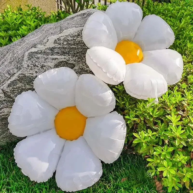 A cluster of white and yellow aluminum foil balloons resting on green grass next to a large gray rock.