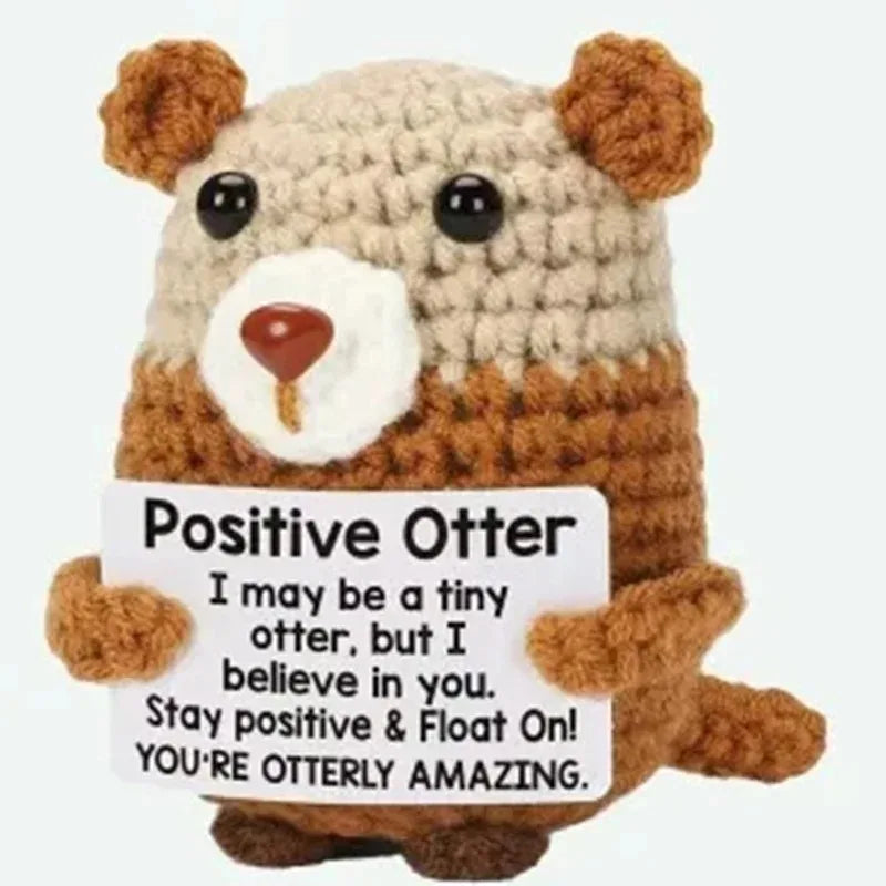 A handmade crochet otter doll with brown fur and white chest holding an inspirational card.