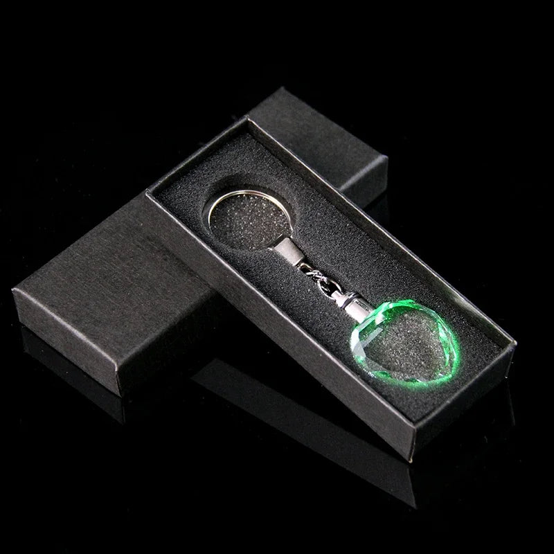 Llavero de cristal en forma de corazón color plateado, mostrado dentro de una caja de terciopelo negro.