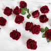 A collection of deep red velvet artificial roses scattered on a white textured fabric.