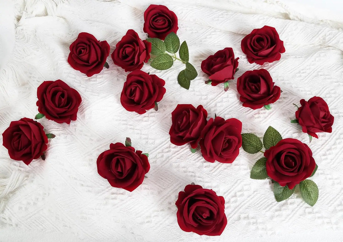 A collection of deep red velvet artificial roses scattered on a white textured fabric.