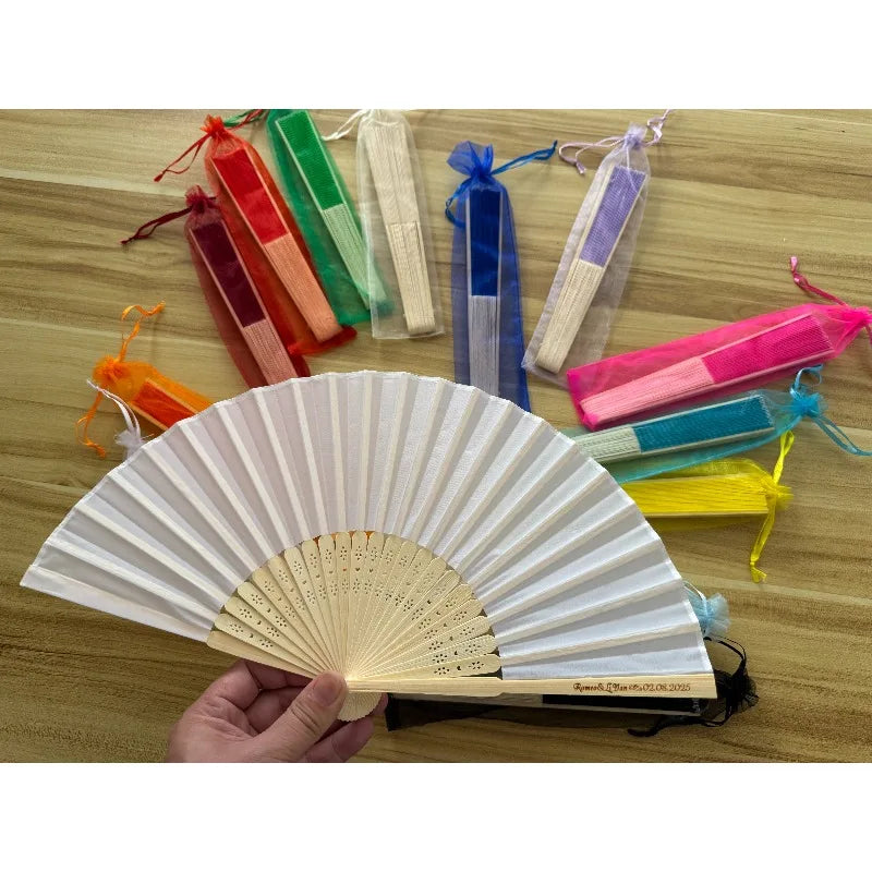 A collection of colorful silk wedding hand fans with bamboo frames displayed on a wooden surface.