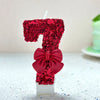 A number seven candle decorated with red glitter and a large red bow on a white base.