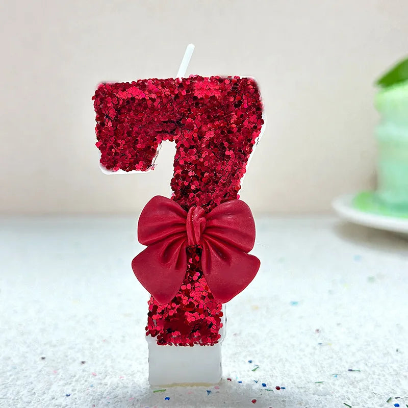 A number seven candle decorated with red glitter and a large red bow on a white base.