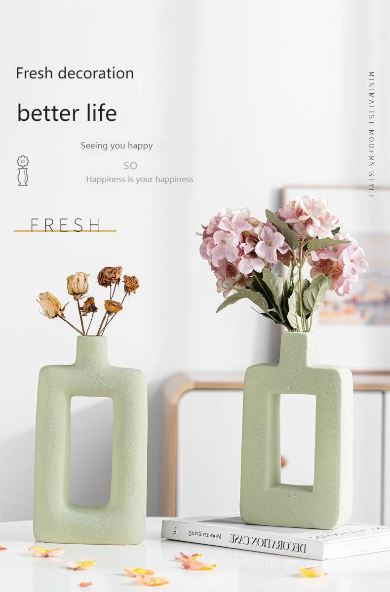 A light green ceramic vase holding pink flowers on a white table.