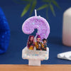 A purple glitter number 9 candle featuring characters from a cartoon set on a white base.