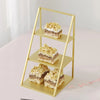 A gold-colored three-tier iron display rack holding three square cakes or pastries.
