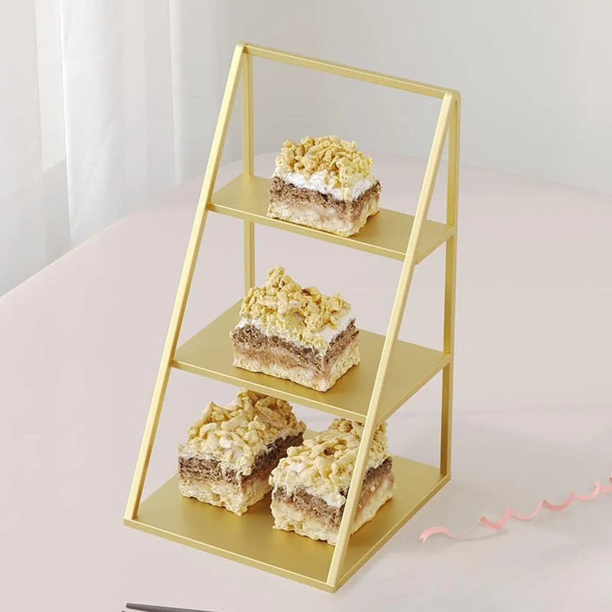 A gold-colored three-tier iron display rack holding three square cakes or pastries.