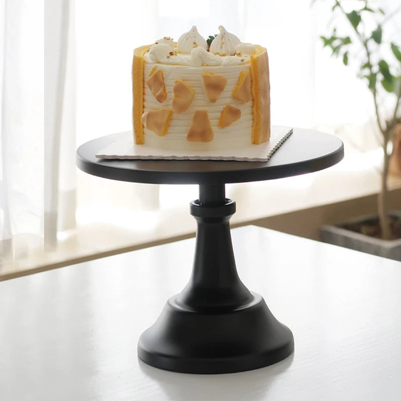 A layered white cake decorated with cream and orange accents displayed on a black metal cake stand.