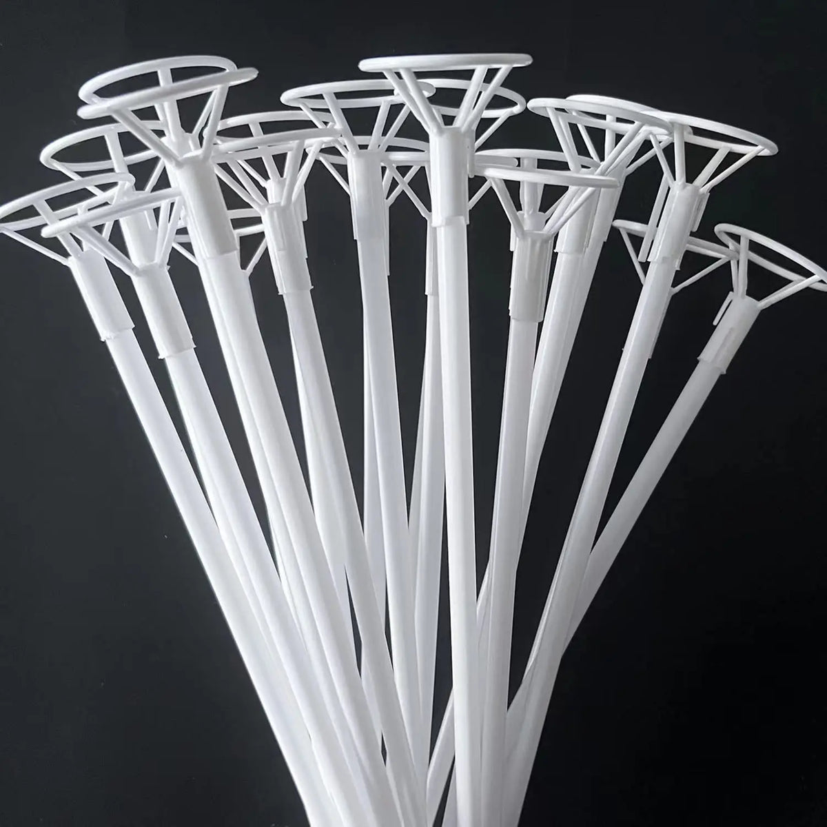 A close-up view of white balloon holder sticks arranged in a fan shape against a dark background.