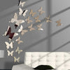 A set of twelve mirror effect butterfly wall stickers displayed on a gray wall above a white tufted sofa.