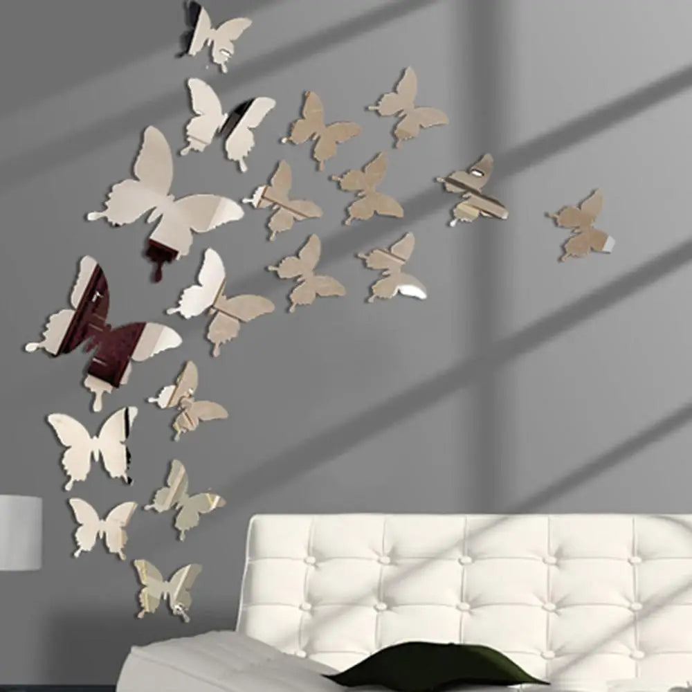 A set of twelve mirror effect butterfly wall stickers displayed on a gray wall above a white tufted sofa.