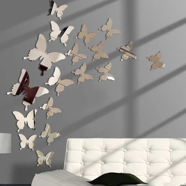 A set of twelve mirror effect butterfly wall stickers displayed on a gray wall above a white tufted sofa.