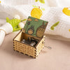 A hand-cranked wooden music box featuring a Totoro design, set against a white fabric with green leaves.