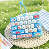 A blue cartoon animal keyboard keycap keychain resting on a knitted surface in a grassy outdoor setting.