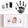 A photo frame displaying black handprint and footprint impressions on white paper, with a separate black handprint above.