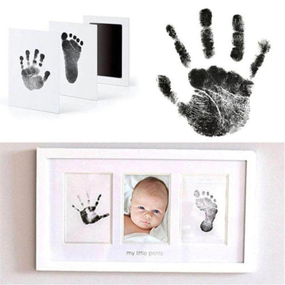 A photo frame displaying black handprint and footprint impressions on white paper, with a separate black handprint above.