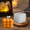 A white silicone mold shaped like a smiling pumpkin is displayed on a wooden surface next to a lit candle and Halloween decor