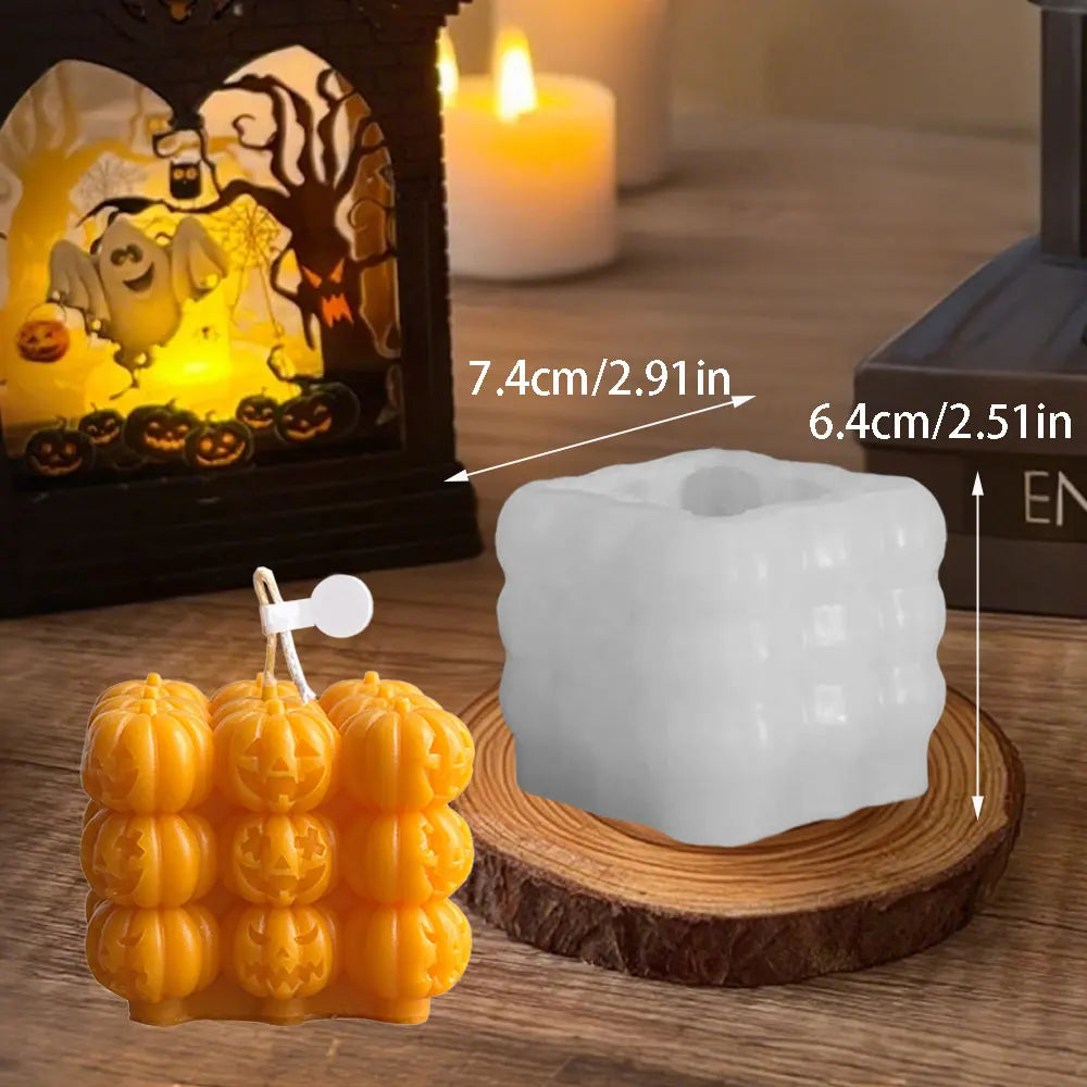A white silicone mold shaped like a smiling pumpkin is displayed on a wooden surface next to a lit candle and Halloween decor