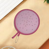 A round pink foldable hand fan with a fruit design is shown on a light wooden surface.