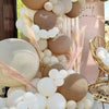 A balloon garland featuring brown and white balloons decorated with dried pampas grass in an outdoor setting.