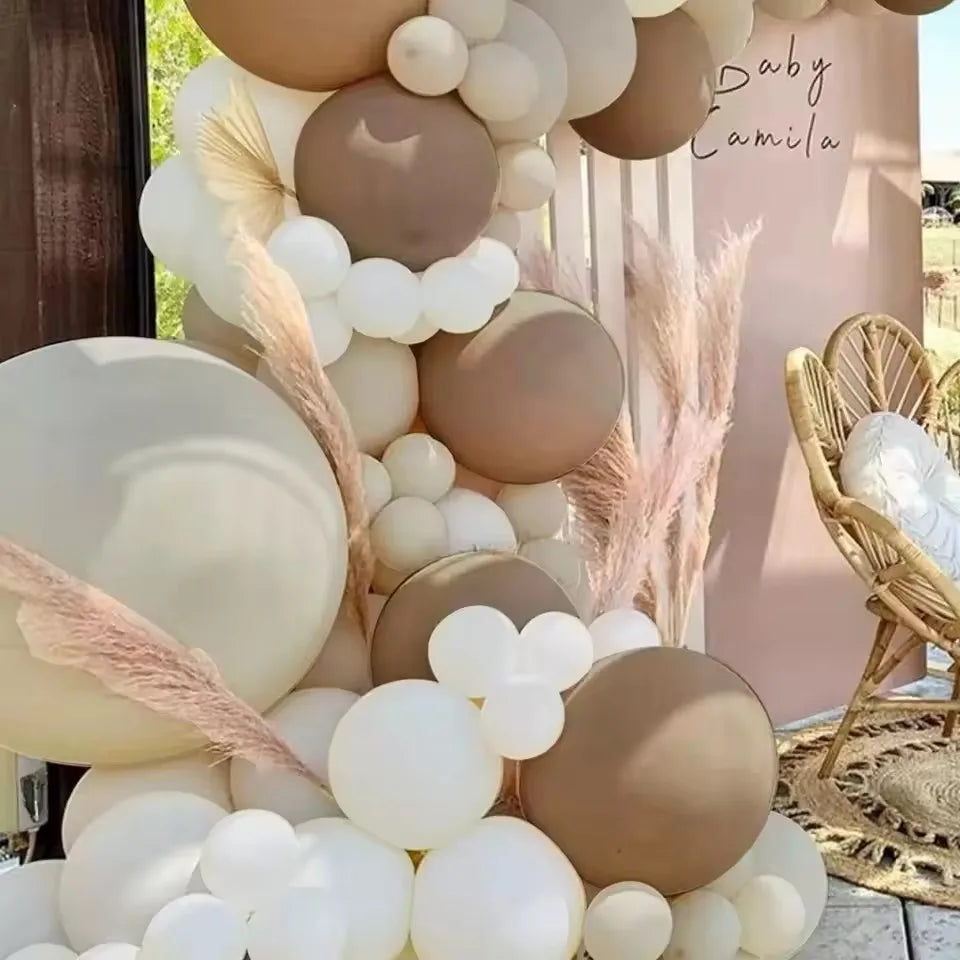 A balloon garland featuring brown and white balloons decorated with dried pampas grass in an outdoor setting.