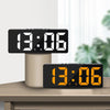 A black LED digital alarm clock displaying 13:06 on a wooden surface.