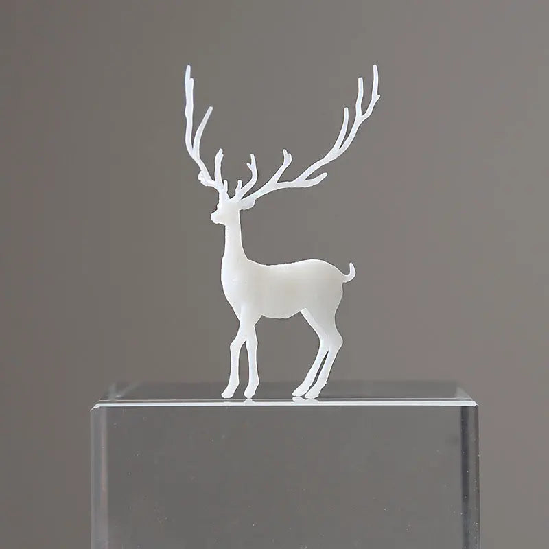 A white resin ornament of an elk deer with antlers standing on a clear glass block.