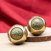 A pair of golden Chinese lucky coin fidget toys resting on a wooden surface with a red fabric background.